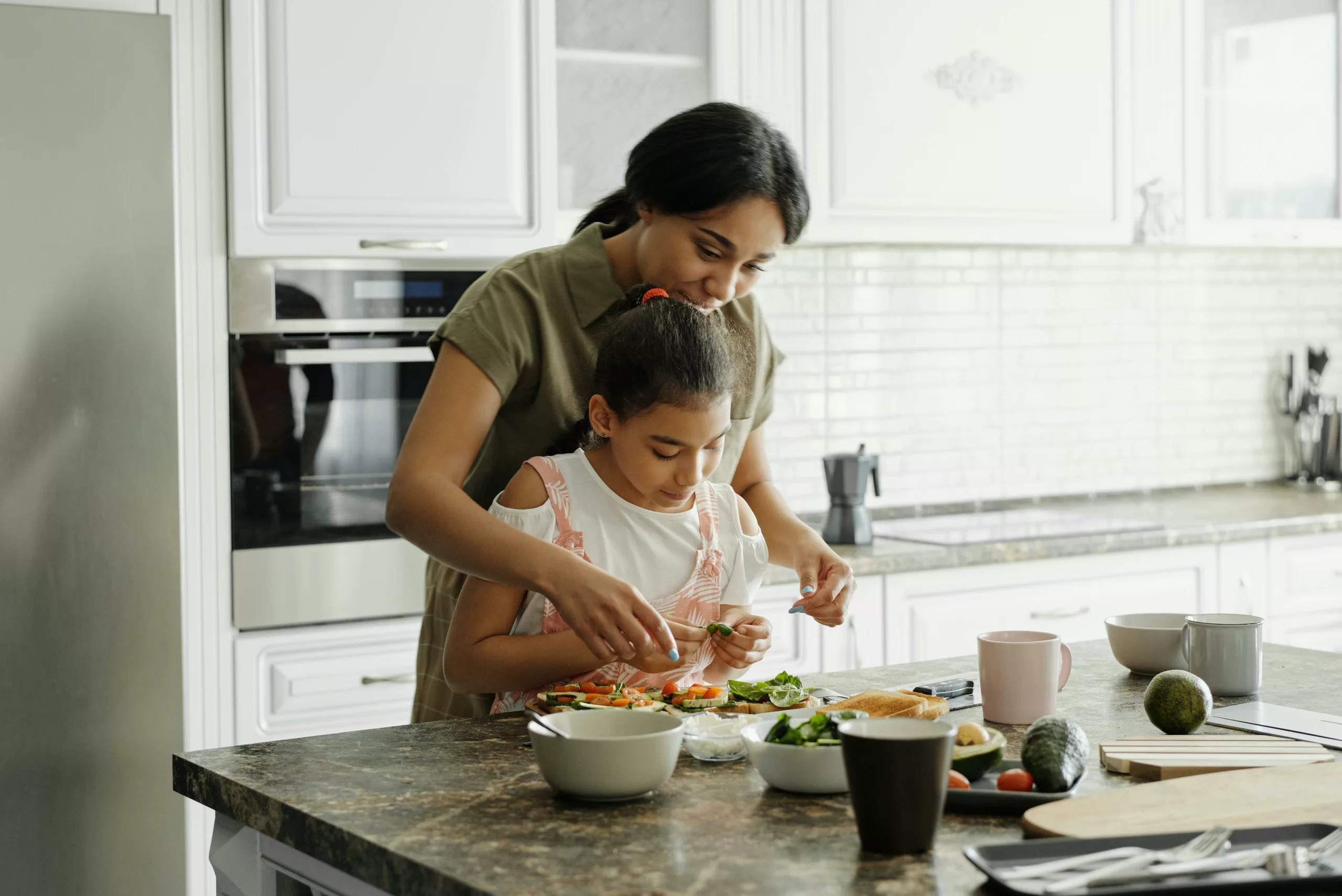 A mother and daughter of color preparing a healthy meal together in the kitchen, surrounded by fresh vegetables and cooking utensils.